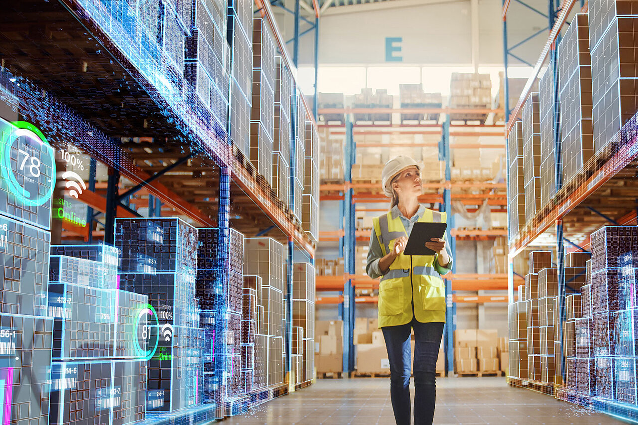 A person with a tablet in a warehouse, standing between shelves fitted with digital displays for stock and process monitoring.