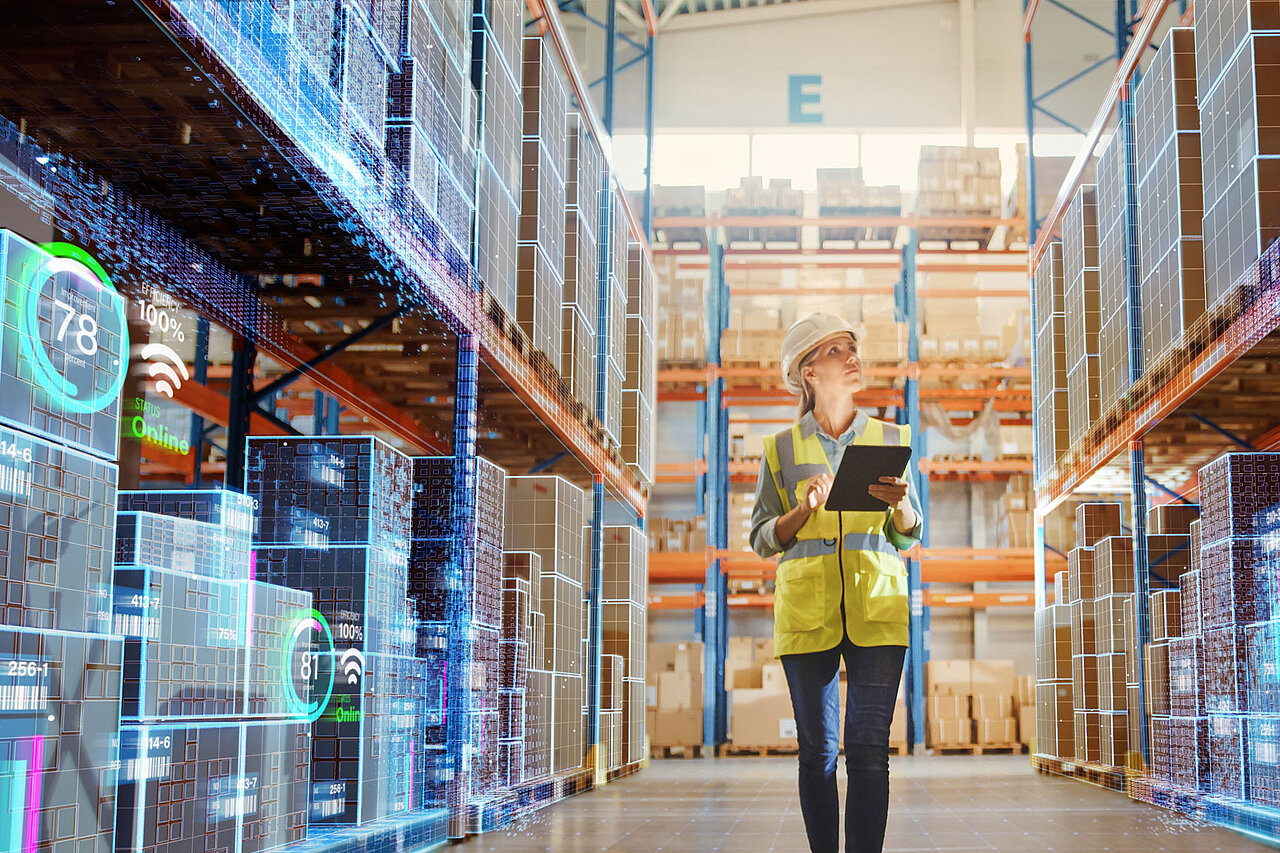A person with a tablet in a warehouse, standing between shelves fitted with digital displays for stock and process monitoring.