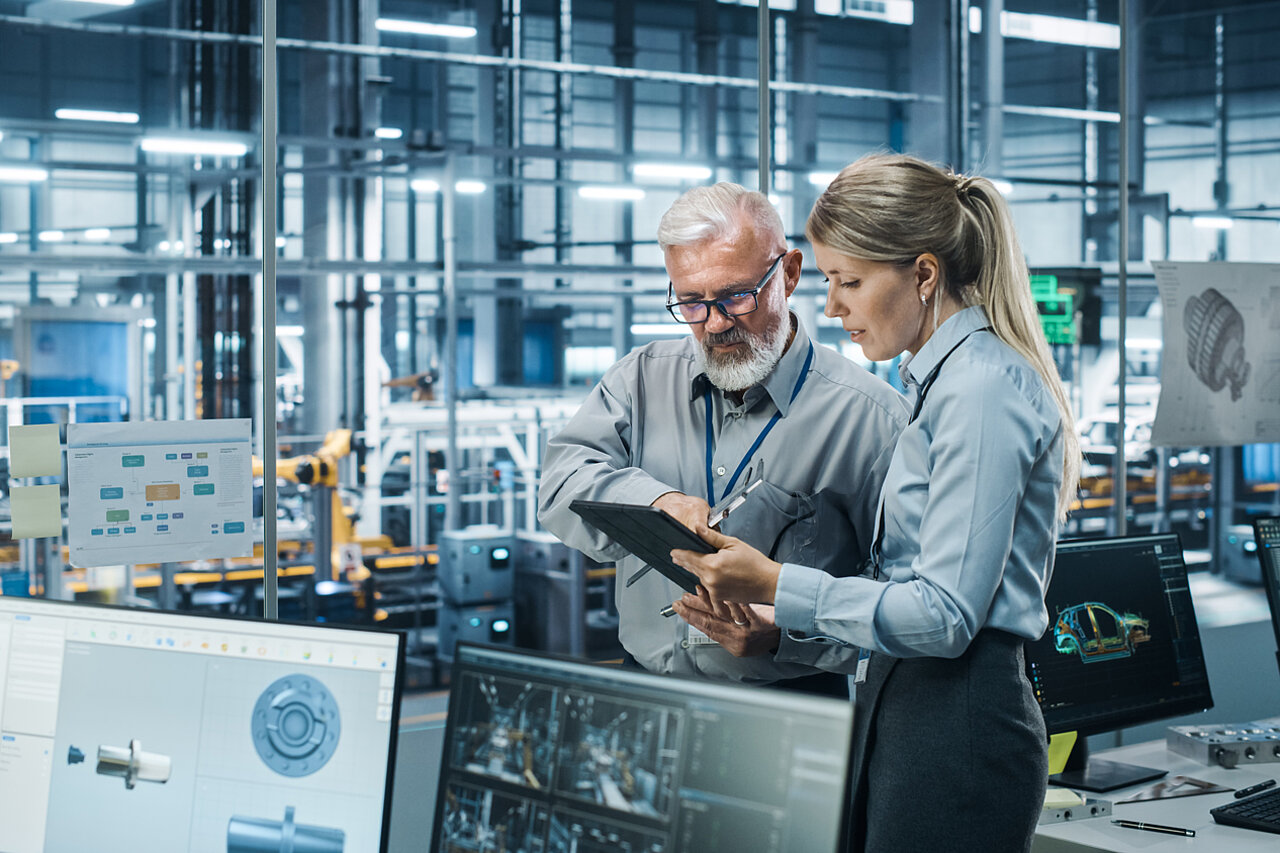 Two specialists are analysing digital production data on a tablet in a modern manufacturing environment to evaluate software solutions and digital use cases.