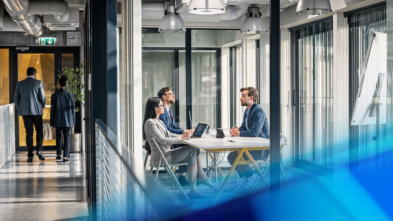 Three people are discussing projects and strategic issues at a meeting table in a modern office.