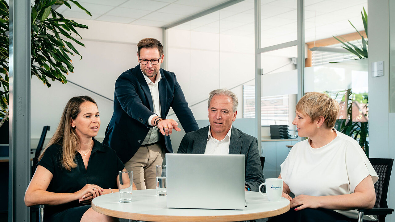 Vier Ingenics Mitarbeitende besprechen Projekte und Aufgaben an einem Besprechungstisch im Büroumfeld.