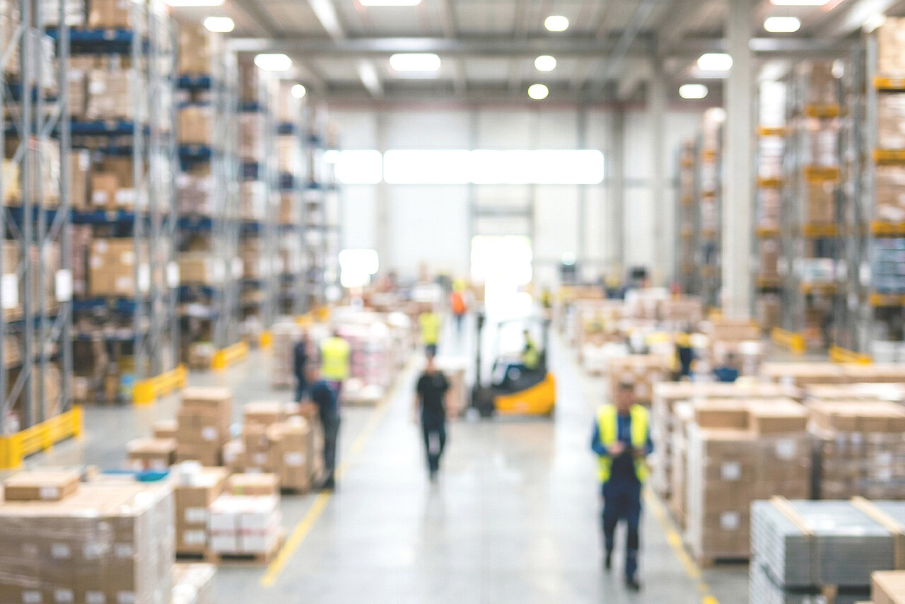 A modern warehouse with high-bay racking, stock and staff in the logistics operation, designed to optimise stock levels and material flows.